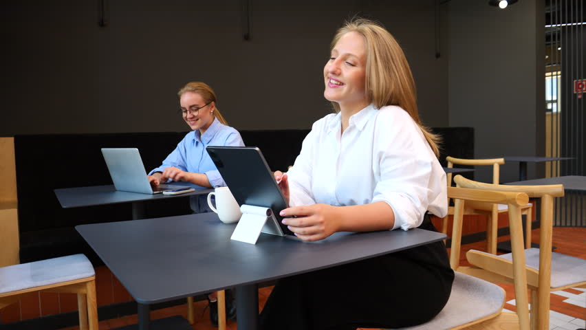 Two people work in a trendy cafe, using their devices and soaking up the lively atmosphere.
