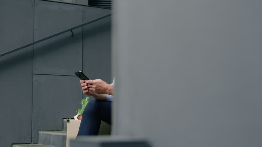 Serious fired unemployed Caucasian middle-aged businessman using smartphone searching work vacancy online thinking business man male guy in city with mobile phone with dismissal box dismiss lost job