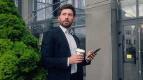 Male manager in city near office drinking coffee looking away relaxed thinking dreaming smiling calm look check time with mobile phone Caucasian man business guy employer businessman run late to work - Powered by Shutterstock - Get 15% off with code: PIKWIZARD15