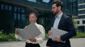 Confident Caucasian man businessman male guy with African American female businesswoman girl business partners talking walking in city downtown hold clipboard with documentation discussing meeting - Powered by Shutterstock - Get 15% off with code: PIKWIZARD15