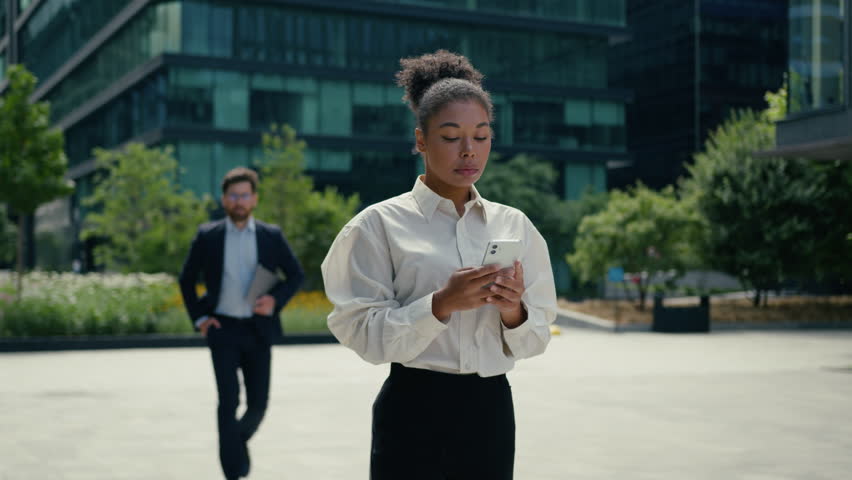 African American woman businesswoman female girl in city walking using mobile phone chat Caucasian man businessman guy male approach walking to lady hugging talking multiethnic business coworkers