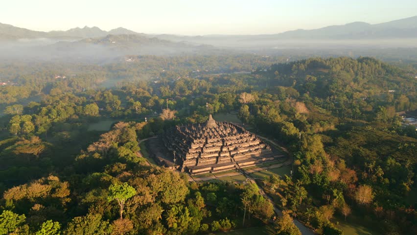 Aerial view of ancient Borobudur temple, surrounded by tropical misty jungle and soft morning light in Central Java, Indonesia.
