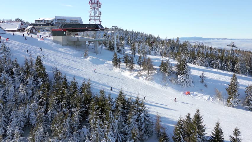 Aerial view of snowy ski resort with people skiing down the slope on a sunny winter day.