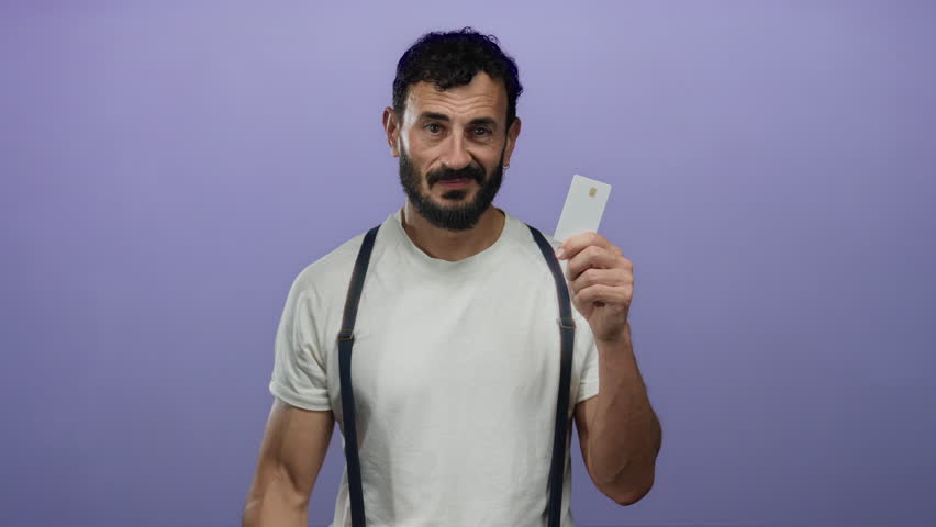 Hispanic man with beard holding credit card against purple background, wearing white shirt and suspenders, gesturing towards head, suggesting thoughtful financial decisions. - Powered by Shutterstock - Get 15% off with code: PIKWIZARD15