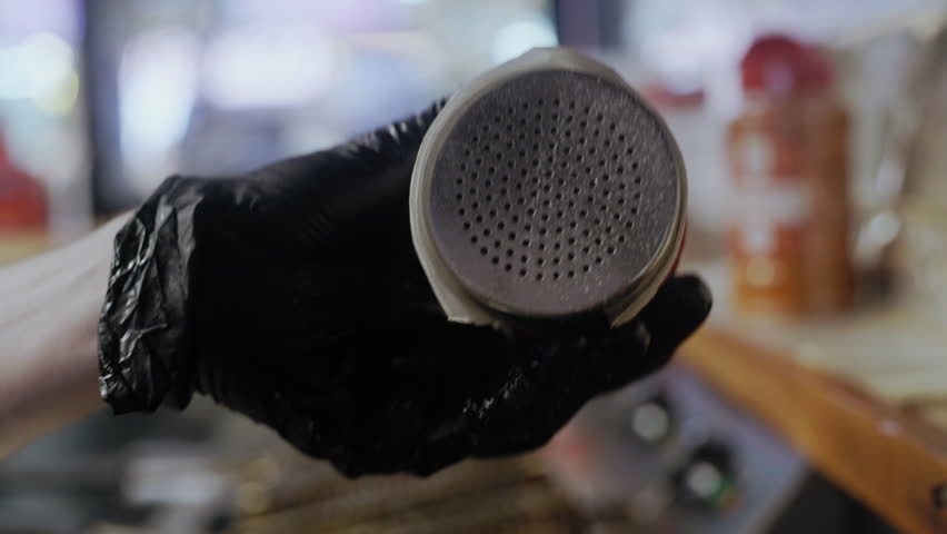 A close-up shot of a chef’s hands sprinkling salt on a smoking meat patty frying on a hot stove.