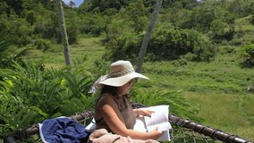 A young woman in a straw hat enjoys a tranquil moment, reading on a hammock. The surrounding rice fields and lush jungle create a soothing atmosphere, slow motion - Powered by Shutterstock - Get 15% off with code: PIKWIZARD15