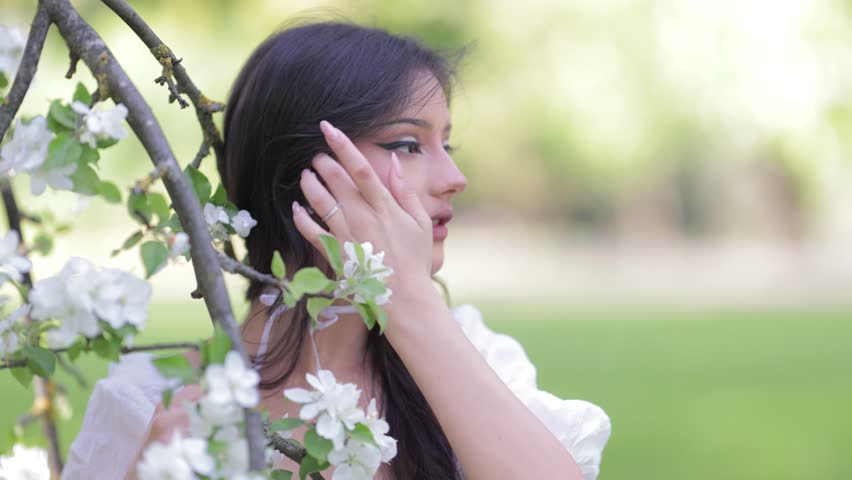 Beautiful Girl with long hair poses near white blossoming apple trees