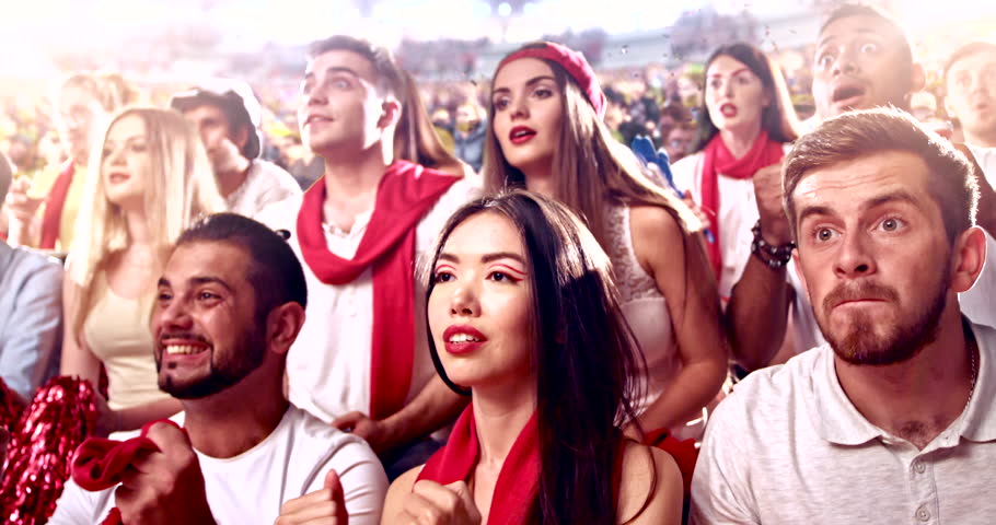 Excited fans cheer passionately during a live sports event, waving hands, shouting, and celebrating together in a vibrant stadium atmosphere