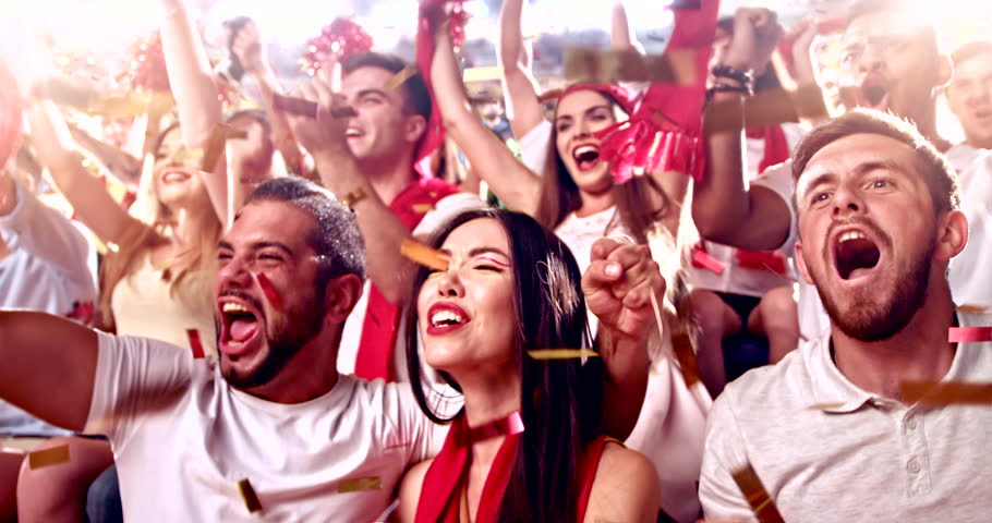 Excited fans cheer passionately during a live sports event, waving hands, shouting, and celebrating together in a vibrant stadium atmosphere