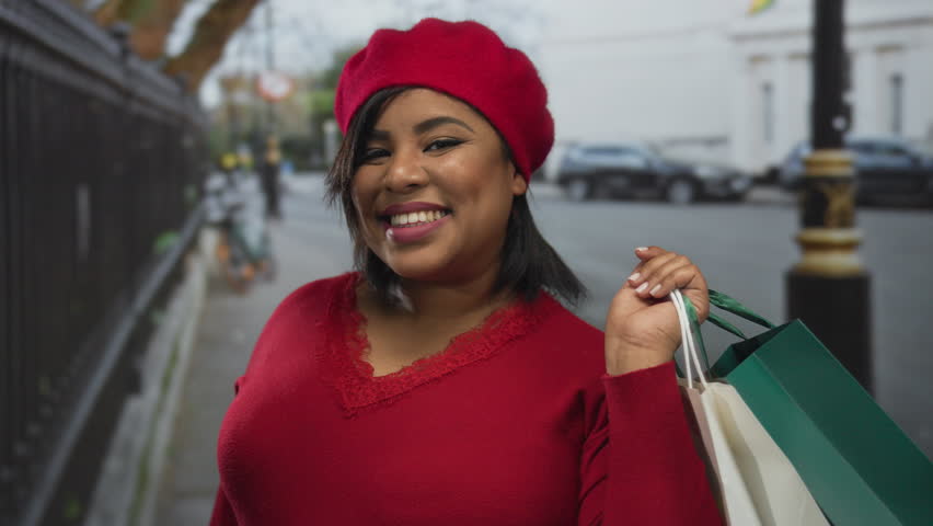 Woman smiling holding shopping bags on city street wearing red hat in urban outdoor setting showcasing plus size fashion.