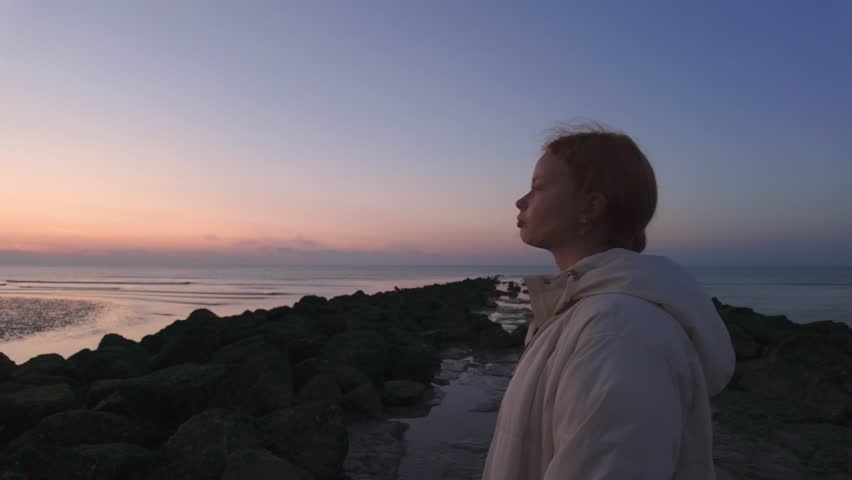 A serene individual peacefully gazes at the beautiful horizon during a vibrant and colorful sunset by the ocean