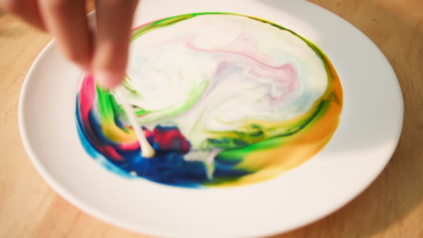 Close-up of dish soap touching milk with food coloring, instantly breaking surface tension and causing a colorful swirl explosion — a fun science activity for kids.