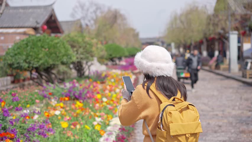 Young female tourist taking a photo of the Lijiang Ancient Town, The famous tourist destination at Yunnan Province, China