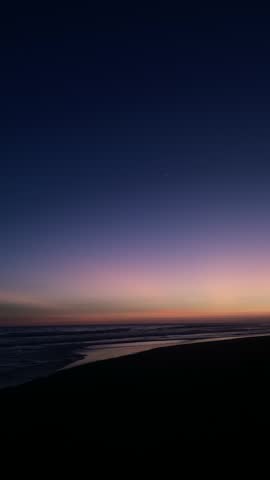 The video captures the beauty of a sunset on the beach, with the sky displaying soft gradients of color from warm orange on the horizon to deep dark blue above.