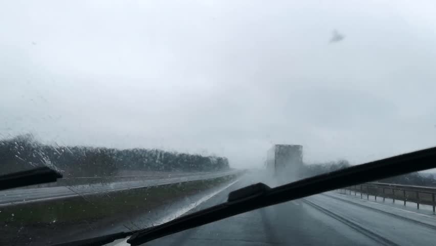 Bad driving conditions on a highway in wet snow and rainy weather. Blurry car front view. Overcast. Traffic. Slippy road. Difficult visibility. The windscreen wiper. Moving automobiles. Speed way.