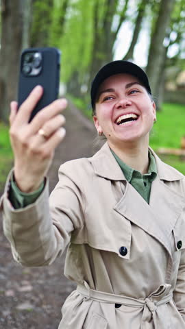 Smiling woman walking in the park in spring clothes, woman in beige trench coat and black blazer, cold season fashion accessories, elegant beautiful lady. Woman walking in the park and enjoying nature