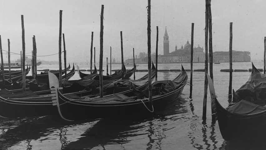 Vintage film-stylised black and white Video of Gondolas moored near San Marco square with a view at San Giorgio Maggiore Church in the background. Venice, Italy.
