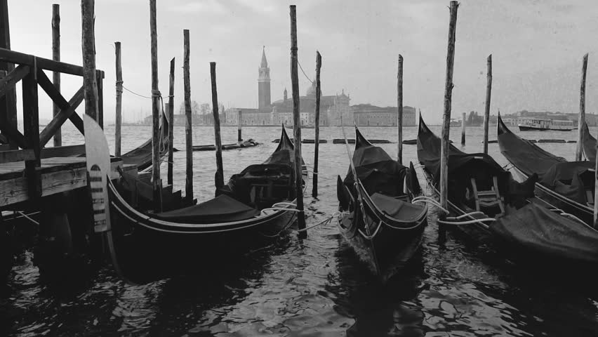 Vintage film-stylised black and white Video of Gondolas moored near San Marco square with a view at San Giorgio Maggiore Church in the background. Venice, Italy.
