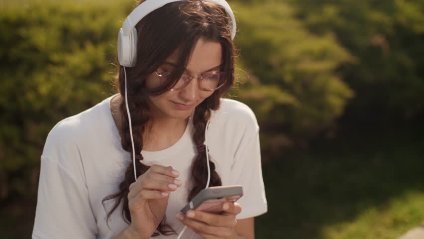 Peaceful girl in glasses and headphones holds a vibrant pink magnolia flower during a spring day outdoors. Ideal for wellness, self-love, youth culture, and lifestyle promos.