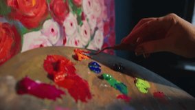 Palette knife wielding creative professional selecting vibrant red oil paint and carefully applying pigmented strokes onto canvas featuring delicate rose composition within art studio setting - Powered by Shutterstock - Get 15% off with code: PIKWIZARD15