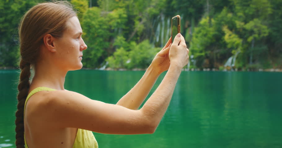 Woman takes photo of turquoise lake and waterfalls at Plitvice Lakes National Park in Croatia