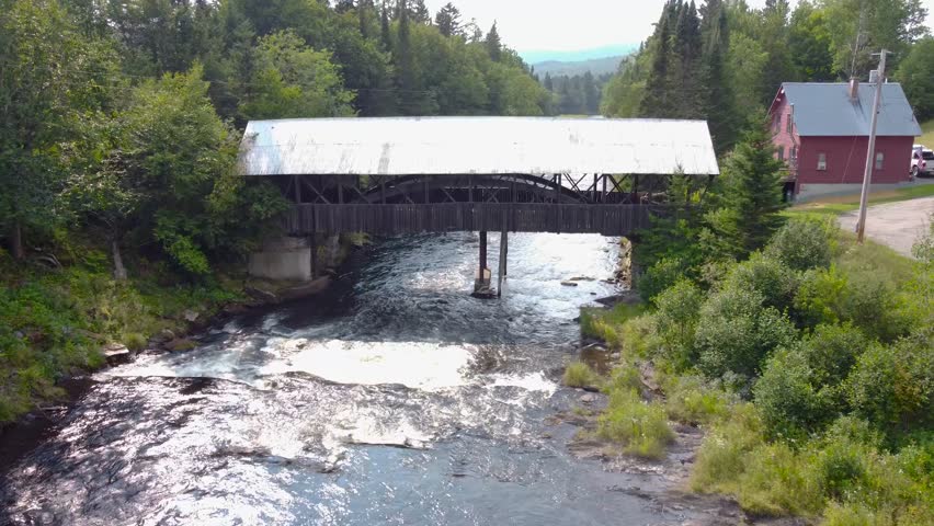 New England Rustic Covered Bridge Over A River in a lush forest. Aerial cinematic video.