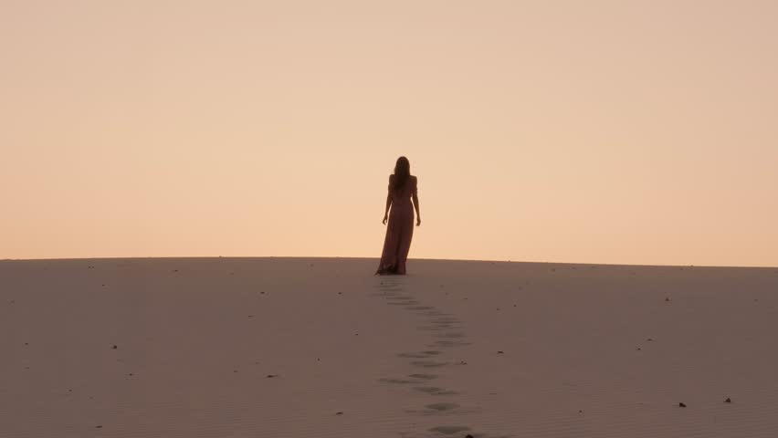 A solitary woman walks toward the glowing sunset on quiet desert dunes, leaving footprints behind her. Stunning silhouette concept for freedom, solitude, and emotional storytelling themes.