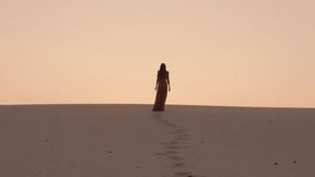 A solitary woman walks toward the glowing sunset on quiet desert dunes, leaving footprints behind her. Stunning silhouette concept for freedom, solitude, and emotional storytelling themes. - Powered by Shutterstock - Get 15% off with code: PIKWIZARD15