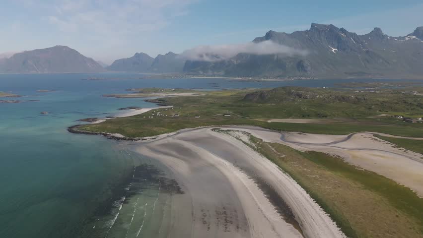 Discover the serene beauty of Lofoten Norway as the camera glides above dramatic coastlines and emerald waters. Lush green hills and towering peaks create a captivating landscape bathed in sunlight.
