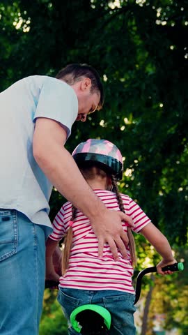 Child cyclist with Father, nature. Family weekend, Father teaches kid daughter to ride bike in park. Happy family, little girl in helmet together with her dad learns to ride bicycle outdoors in summer