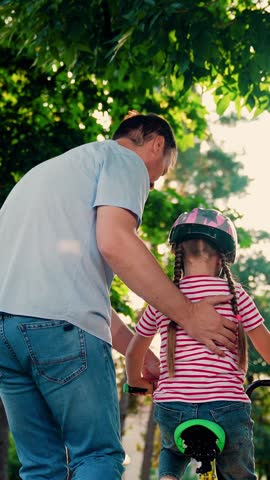Child cyclist with Father, nature. Family weekend, Father teaches kid daughter to ride bike in park. Happy family, little girl in helmet together with her dad learns to ride bicycle outdoors in summer