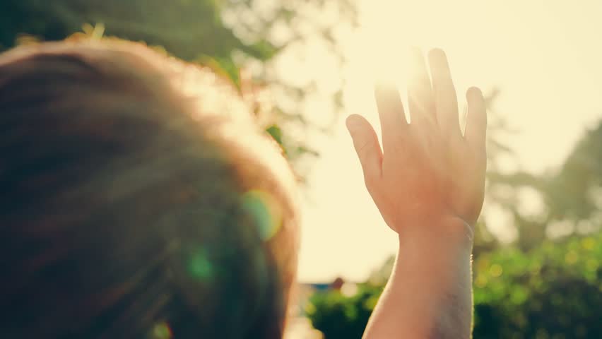 Sunlight, fingers. Sunlight in child's hands, outdoors. Happy child boy raises palm to sun. Child dreams in park against sun. Child prayer, boy stretches hands to sun. Religion. Little girl plays park