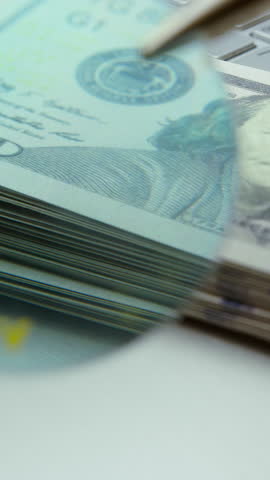 Close-Up of Counterfeit Money Inspection with Ultraviolet Light on Dollar Bills Over Laptop ,vertical video