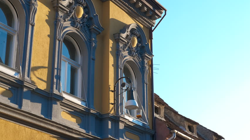 Elegant yellow building with grey window frames. Sunlight illuminates a yellow building with ornate grey window frames, showcasing intricate architectural details