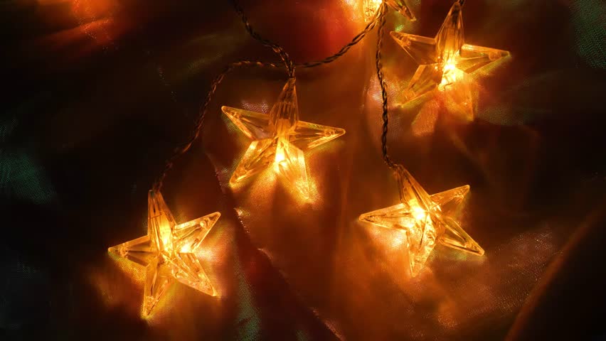 Star garland and iridescent fabric.Warm light of garlands in the dark and gradients of shiny fabric.Christmas beautiful background. Cozy festive warm atmosphere. 4k footage