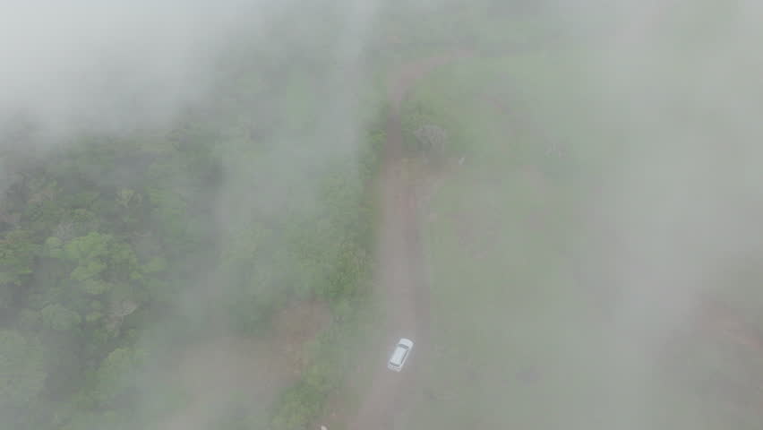 An adventurous SUV navigates picturesque meadows enveloped in soft clouds and fog, showcasing the natural beauty of Costa Rica in stunning 4K aerial footage that captures the essence of the landscape