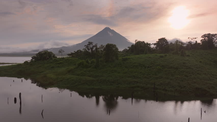 Experience breathtaking aerial views of a stunning sunrise over Laguna de Arenal and Volcan Arenal in Costa Rica, showcasing lush forests and misty landscapes that evoke serenity and tranquility