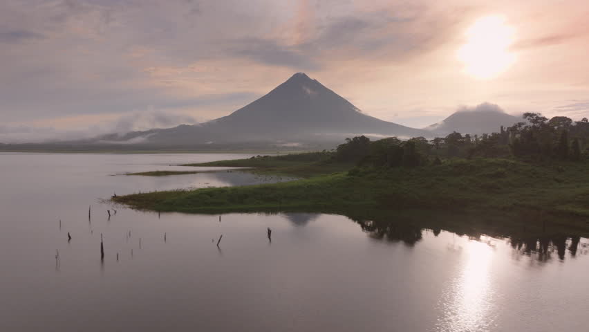 Experience breathtaking aerial views of a stunning sunrise over Laguna de Arenal and Volcan Arenal in Costa Rica, showcasing lush forests and misty landscapes that evoke serenity and tranquility