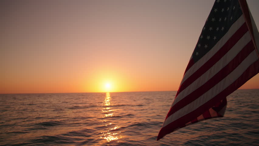 Experience the stunning views of an American flag waving on a sailing ship at sunset in Key West, Florida. This vibrant sunset evokes a sense of tranquility and unforgettable peace