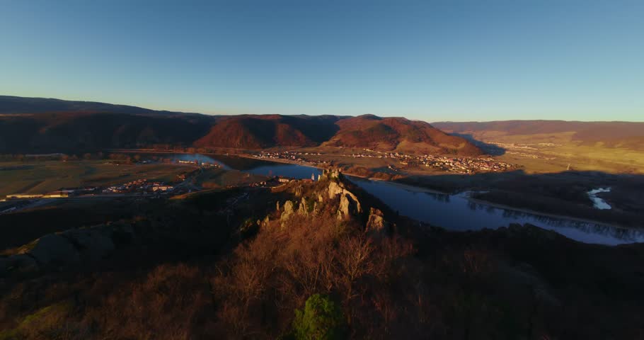 FPV pov drone shot of Dürnstein’s medieval castle ruins atop sunlit cliffs in Wachau Valley with Danube flowing below, with distant vineyards and villages nestled in the golden hills of Lower Austria.