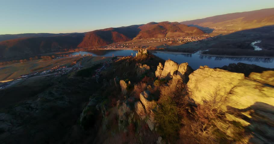 High-speed wide-angle FPV drone captures thrilling descent over Dürnstein Castle ruins, revealing the Danube River, Wachau hills, and nearby vineyards bathed in golden hour light.