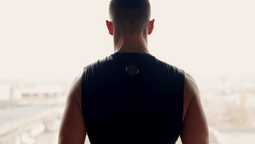 Backlit silhouette of a muscular man flexing his arms, showcasing strength and fitness against a well-lit window backdrop. Strong Athletic Man Flexing Muscles in Silhouette Against Window
