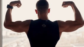 Backlit silhouette of a muscular man flexing his arms, showcasing strength and fitness against a well-lit window backdrop. Strong Athletic Man Flexing Muscles in Silhouette Against Window - Powered by Shutterstock - Get 15% off with code: PIKWIZARD15