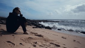 On a sunny summer day, a thoughtful, young guy rests on an empty sandy beach.  On a beautiful day, a man sits on a sandy beach.  Man in a romantic mood on the beach, looking out at the gorgeous ocean - Powered by Shutterstock - Get 15% off with code: PIKWIZARD15