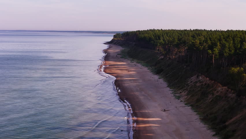 Aerial of Jurkalne coast showing forest edge, bluff, and calm water at golden hour