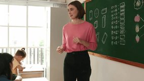 Skilled caucasian teacher looking at african girl writing answer on blackboard at elementary school. Professional student walking at in front of class to answer quiz in elementary classroom. Pedagogy. - Powered by Shutterstock - Get 15% off with code: PIKWIZARD15