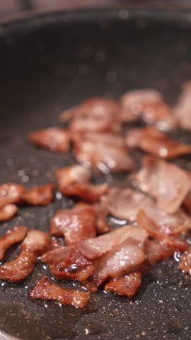 A pan of bacon is sizzling in a skillet. The bacon is cooked and crispy, with some pieces still slightly pink. The skillet is full of grease, and the bacon is scattered all over the pan