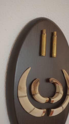 A wooden plaque with a design of a wild boar horns trophy, with two tusks and two bullets on it