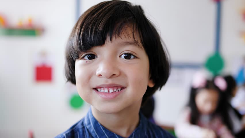 Happy Asian kid smiling at camera inside school classroom. Preschool student face portrait
