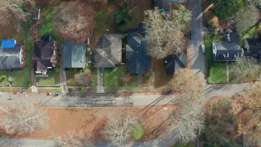 A slow overhead panning down a row of scenic and historic single family homes, with yards in the front and back, under the shade of the beautiful fall tree canopy in Atlanta, Georgia.